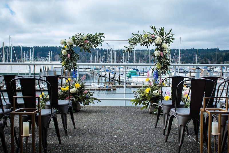 Chairs in two separate rows creating an aisle between them looking towards the water and an flowery arch