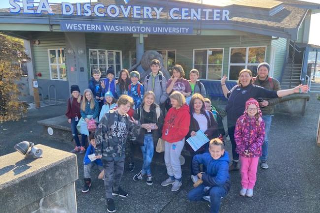 A group of children and adults standing in the sunshine outside of the Sea Discovery Center